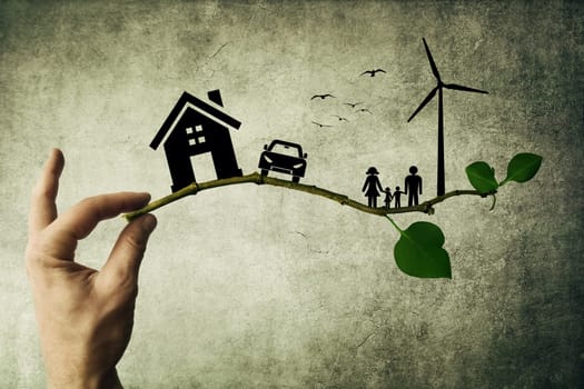 Human hand holding a tree branch. Environmental green energy concept. Silhouette of happy family, house, car and windmill