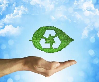 Opened hand holding a green leaf with recycling symbol on a blue sky background. Friendly environment and sustainable development concept