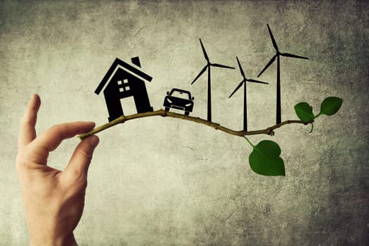 Human hand holding a tree branch. Environmental green energy concept. Silhouette of house, car and wind turbine