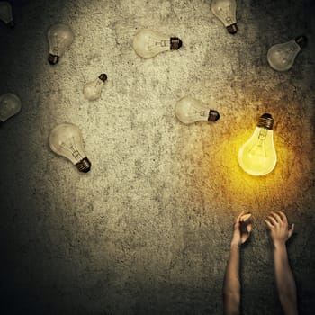 Abstract idea concept as human hands stretched out and juggling with a lot of lightbulbs, one of them glowing. Good idea concept, wealth and success. Inspiration and imagination.