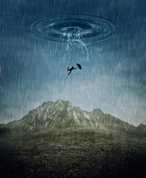 A silhouette of an young man with an umbrella falling from the rainy sky as a splash of water crashing down to the cracked desert ground. Business risk, fail and loss concept