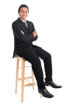 Full body portrait of handsome young Southeast Asian businessman sitting on high chair, isolated on white background.