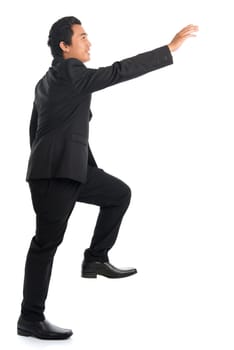 Full body side view of attractive young Southeast Asian businessman stepping up stair case and hand reaching something, isolated on white background.