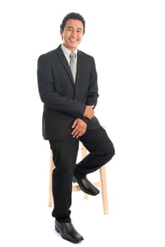 Full body portrait of young Southeast Asian businessman sitting on high chair, isolated on white background.
