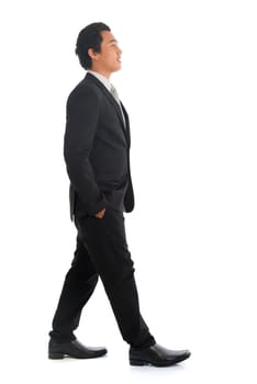 Full length side view of good looking young Southeast Asian businessman walking, isolated on white background.