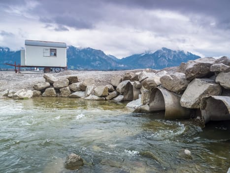 Emptied Forggensee with tree stump and pipes with flowing river Lech near Füssen / Bavaria. The Forggensee is fed by thawing snow from the high Alps and is a reservoir for sedimentary rocks. In spring,the lake is emptied to remove the sedimentary rock. In summer,the lake has returned to its normal water level and is navigated by excursion boats.