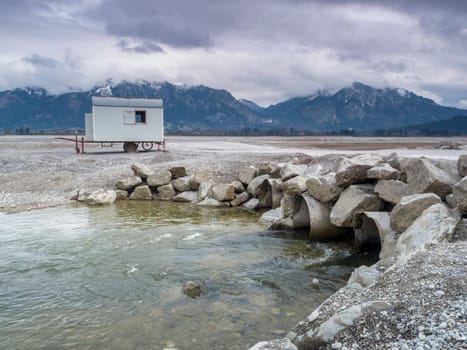 Emptied Forggensee with tree stump and pipes with flowing river Lech near Füssen / Bavaria. The Forggensee is fed by thawing snow from the high Alps and is a reservoir for sedimentary rocks. In spring,the lake is emptied to remove the sedimentary rock. In summer,the lake has returned to its normal water level and is navigated by excursion boats.