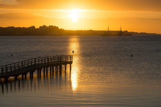 Beautiful sunrise in the summer over old wooden bridge and silent glossy sea. Sunrise over the sea. Pier on the foreground. Panorama