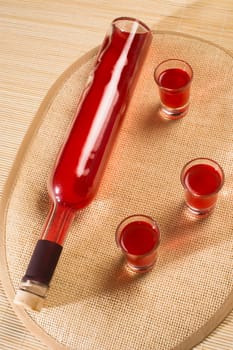 Bottle and three glasses with red alcohol.