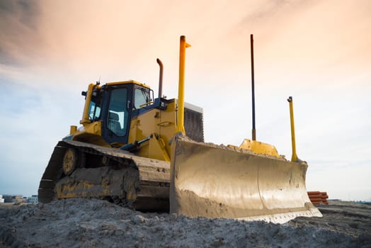 yellow excavator on a construction site in front of an orange sky