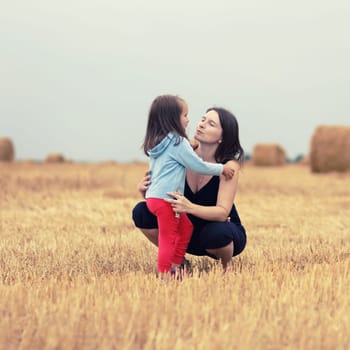 Mother and her daughter child girl hugging in the field against straw bales background. Selective focus on the models. Toned image.