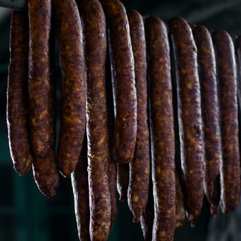 Fresh raw sausages are hanging on dark background.