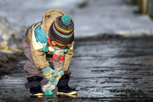 The little child is playing in the puddle at winter.