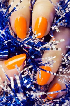 Female hand with orange nails holds blue textured decoration.