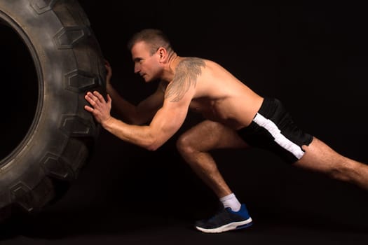 The sportsman pushes a big tractor tire on black background.