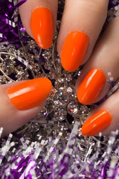 Orange nails on purple and silver texture background.