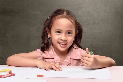 Cute asian little girl drawing on white paper against blackboard background