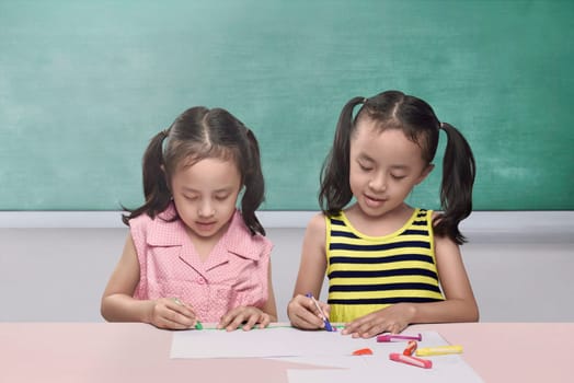 Pretty asian children drawing together on sheet of paper against chalkboard background