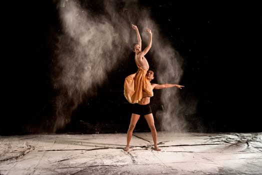 Young couple ballet dancing with powder in the stage against black background