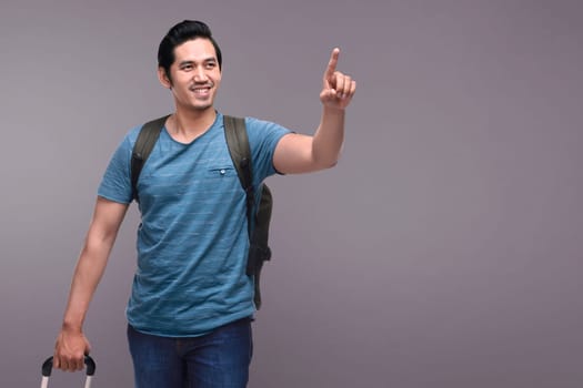 Young asian tourist carrying backpack and suitcase over dark background