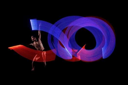 Young man ballet dancing with blue and red lights effect agaisnt black background