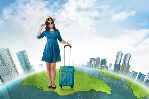 Young asian tourist with suitcase wearing hat standing on the world map