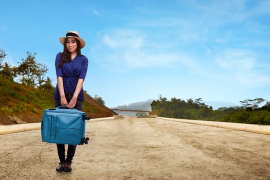 Pretty asian traveler with hat holding suitcase on the street