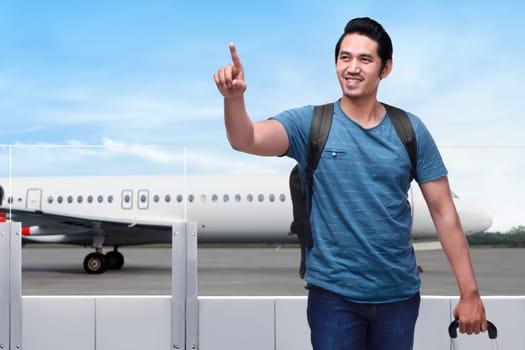 Traveler asian man with bag holding suitcase and pointing with airplane on the background
