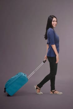 Pretty asian traveler woman carrying suitcase against dark background