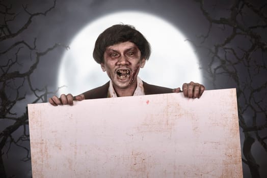 Scary asian zombie man with wounded face with empty banner at dark night