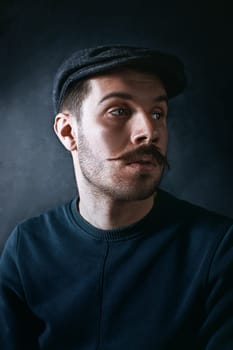 The young man in cap looking away on black background