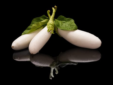 Three white eggplants with water drops and green leaves isolated on black with real reflection
