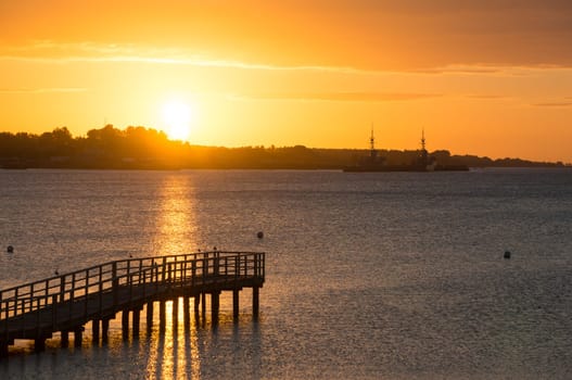 Beautiful sunrise in the summer over old wooden bridge and silent glossy sea. Sunrise over the sea. Pier on the foreground. Panorama