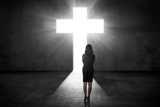 Business woman looking the shining cross on the wall. Religious concept