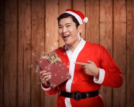 Handsome asian man wearing costume as santa claus, holding gift box