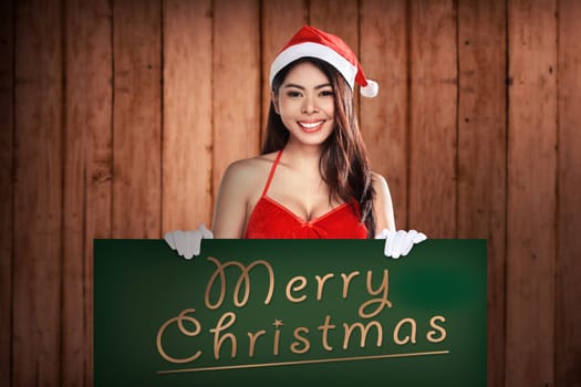 Young attractive asian woman wearing Santa Claus costume holding billboard with merry christmas writing