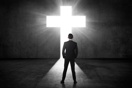 Business man looking the shining cross on the wall. Religious concept