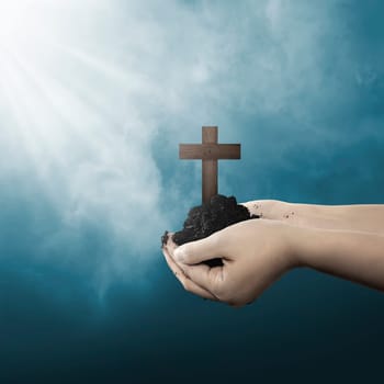 Human hand holding christian cross with soil on the hand over blur background