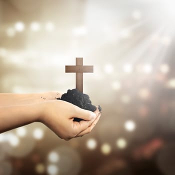 Human hand holding christian cross with soil on the hand over blur background