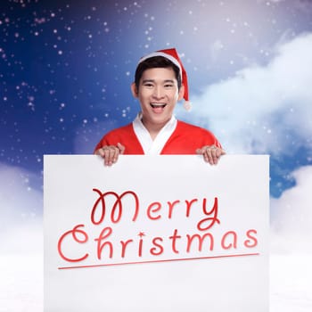 Asian man wearing santa claus costume holding banner with merry christmas writing