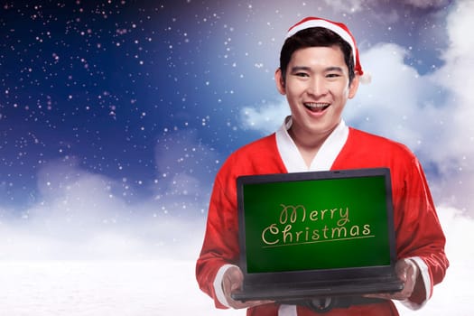 Handsome asian man wearing costume as santa claus and holding laptop with merry christmas writing