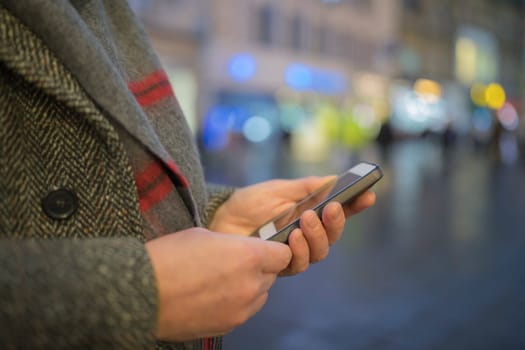 Close up of males hands texting on mobile phone outdoors on the highstreet during winter.
