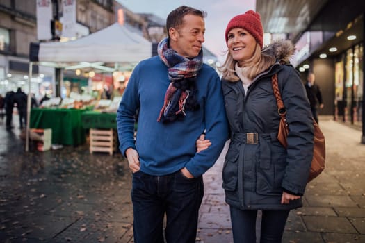 Mature coup le are enjoying an evening stroll through the city christmas market.