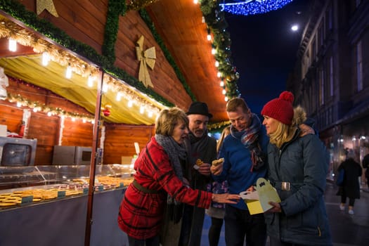 Mature friends are at a christmas market in the city. They are sharing some festive pastries that they have bought from one of the stalls.