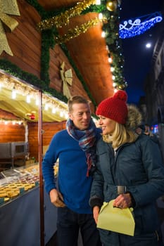 Mature couple are looking at a french pattisserie stall together in the city christmas market.
