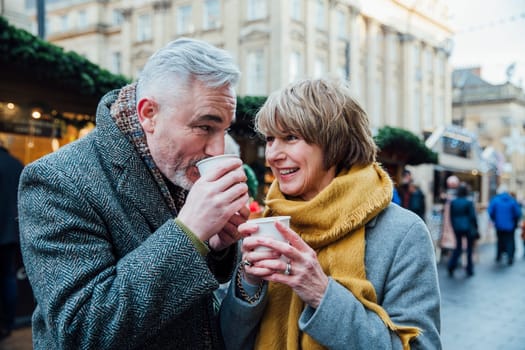 Mature couple are drinking hot drinks in a town christmas market.