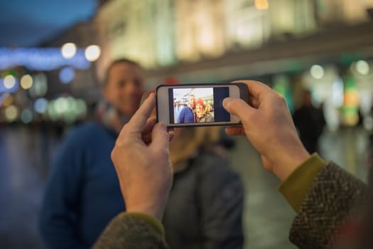 Point of view shot of a smart phone being used to take a photo of adults in the festive city centre at christmas time.