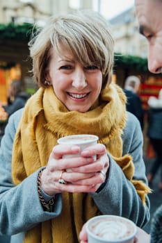 Happy mature woman is smiling for the camera while drinking a hot chocolate in the christmas market.