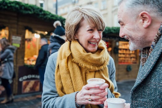 Mature couple are enjoying a cup of coffee as they explore the town christmas market.