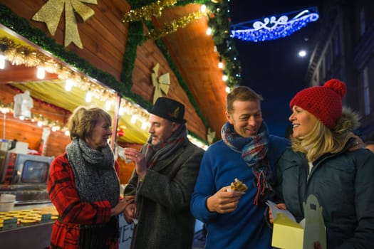 Mature couples are at a christmas market in the city. They are sharing sweet waffles that they have bought from one of the stalls.